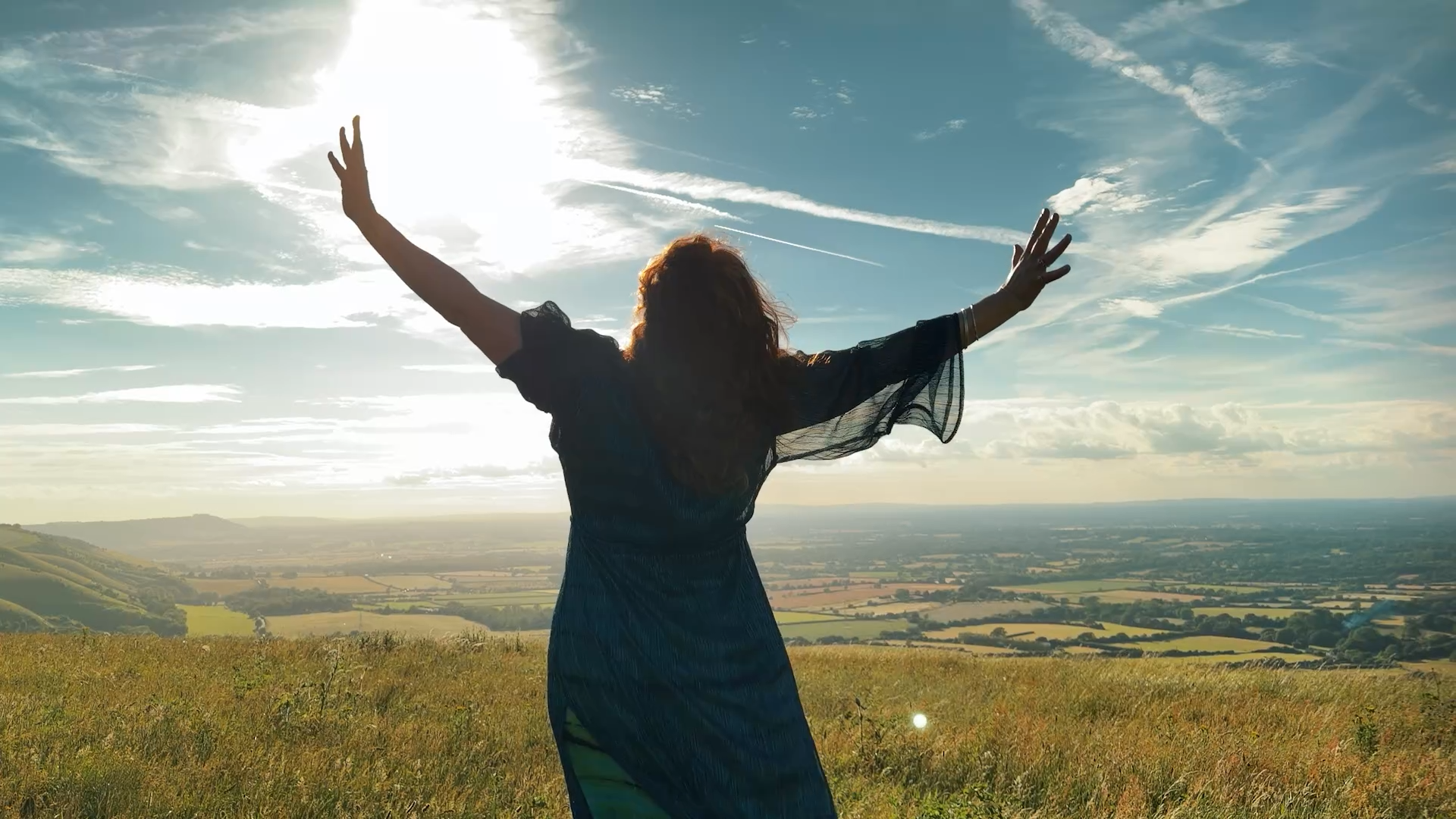 TJ Davis on a hilltop with her arms open to the sun, from the I'm Here video